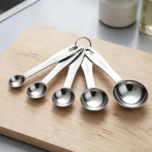 Detailed view of stainless steel measuring spoons set with engraved size markings on wooden board.