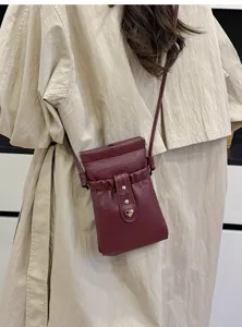 Burgundy leather crossbody phone bag detail shot, compact mini pouch with metal heart buckle.