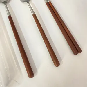 Dettaglio di posate in acciaio inossidabile con manico in legno, design minimal.