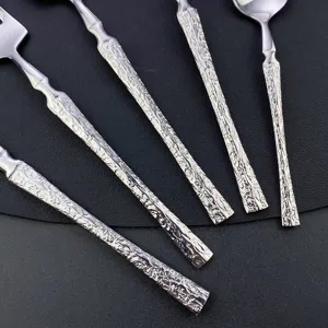 Close-up detail of stainless steel tableware with unique tree texture handles for dining.