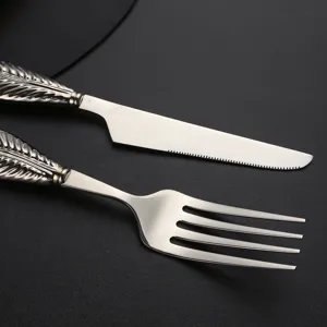 Stainless steel fork and knife set detail shot, featuring elegant feather handle design.