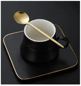 Close-up of black and gold ceramic coffee cup saucer and textured gold spoon set detail.