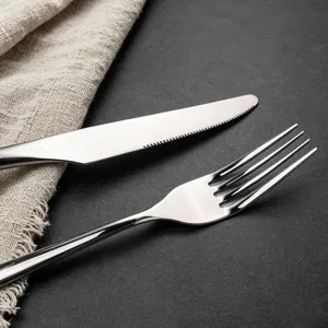 Close-up detail of stainless steel steak knife and fork on dark texture surface with linen.