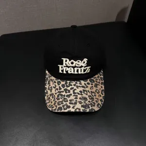 Gorra de béisbol negra con visera de leopardo y letras bordadas en blanco para estilo.