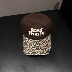 Vista detallada de la gorra de béisbol marrón con visera de leopardo y bordado blanco.