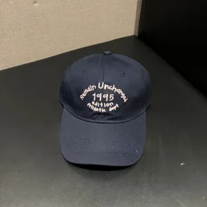 Detail shot of a navy blue baseball cap with pink embroidered text on the front soft crown.