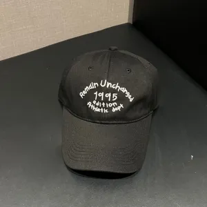 Detailed close-up shot of the black embroidered baseball cap showing the front lettering.