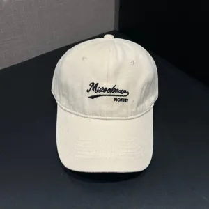 Close-up detail of the beige baseball cap with black embroidery logo and soft crown design.