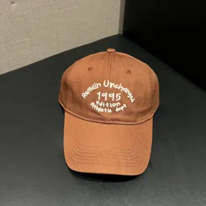 Close-up view of brown baseball cap featuring white embroidery text detail and soft crown.
