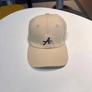 Detail view of khaki baseball cap with navy blue embroidered letter A on cotton twill fabric.