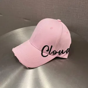 Close-up of pink baseball cap with distressed brim and black Cloud embroidery detail.