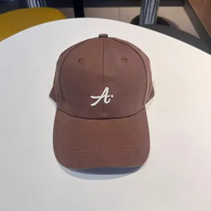 Detail view of the brown baseball cap featuring white cursive letter A embroidery on the front.
