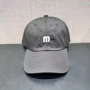 Close-up detail shot of a dark grey baseball cap with a white embroidered letter m on front.