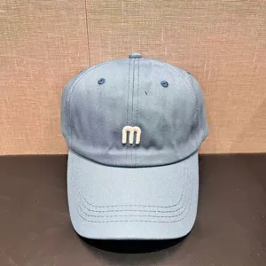Close-up detail of the light blue baseball cap featuring a stylish white embroidered letter m.