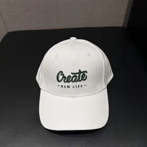 White baseball cap detail view, green embroidered Create text, casual sunshade hat close-up.