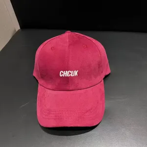Red suede baseball cap detail view showing white embroidered letter design on front.
