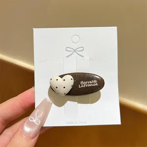 Vista dettagliata della molletta per capelli marrone glitterata con cuore a pois e lettere chic.