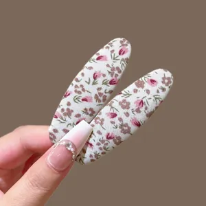Detalle de pinza para el cabello de tela floral retro, forma ovalada con diseño rosa.