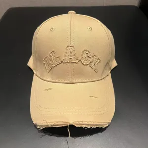 Close-up detail shot of khaki distressed baseball cap with embroidered black text design.