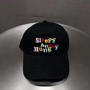 Close-up detail of black baseball cap featuring colorful embroidered letter text and eyelets.