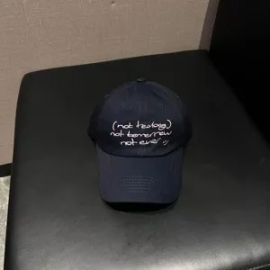 Detailansicht der gewaschenen Jeans-Baseballcap mit weißer bestickter Textgrafik vorne.