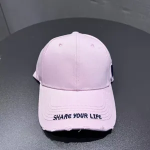 Close-up detail of the pink baseball cap featuring embroidered text on the curved brim.