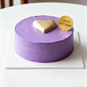 Gros plan d'un gâteau d'anniversaire violet avec cœur doré et topper sur table blanche.
