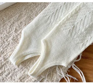 Close-up detail of white knitted stirrup leg warmers showing fine texture and soft cotton fabric.