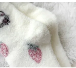 Primo piano di calzini da donna in morbido peluche bianco con motivi di fragole e zampe di gatto.