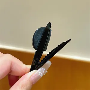 Dettaglio molletta per capelli nera a becco d'anatra con design carino e struttura in metallo per stile.
