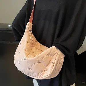 Pink quilted dumpling bag detail view showing delicate bow embroidery and soft padded texture.