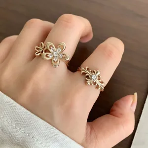 Vue détaillée de bagues strass dorées à motif floral et croix gothique sur une main.