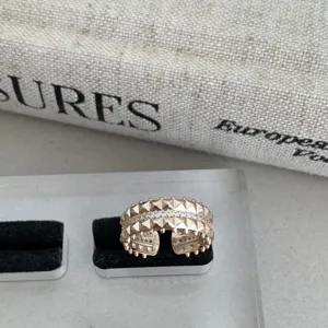 Bague ouverte plaquée or rose avec des détails de clous et un pavé de pierres brillantes.