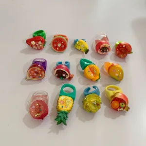 Gros plan des détails de bagues de fruits en résine colorée Y2K, avec fraise, banane et ananas strass.