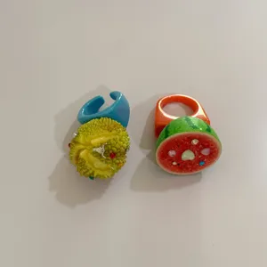 Gros plan détaillé de bagues fruitées en résine chunky avec strass étincelants style tropical.