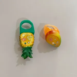 Gros plan de bagues larges tendance en résine avec motifs ananas et mangue tropicaux.