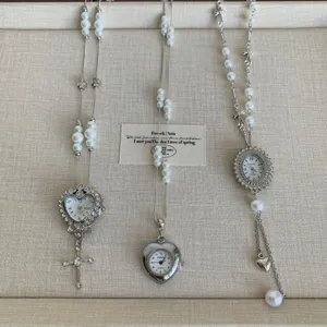 Close-up detail of pearl pendant sweater chain with vintage watch dial and cross charm.