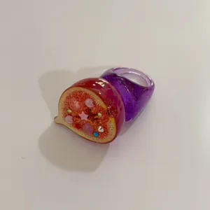 Gros plan sur la bague en résine fruit de figue fantaisie avec strass et bracelet violet.