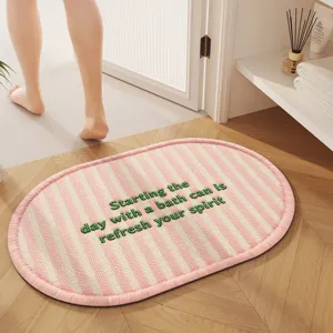 Oval pink white striped bath mat with green embroidered text detail in a cozy home bathroom