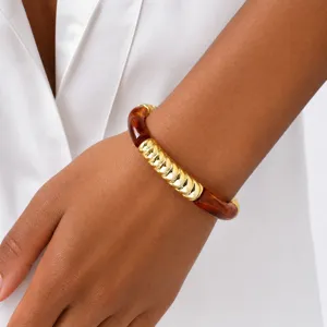 Primer plano detallado del elegante brazalete de tubo de resina ámbar y tono dorado en la muñeca.