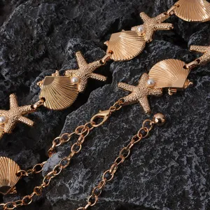 Close-up detail shot of a gold metal waist chain featuring seashell, starfish and pearl accents.