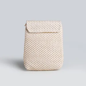Woven straw phone bag close-up detail, showing fine texture, flap closure and metallic ring.