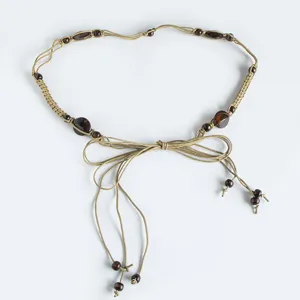 Close-up detail of bohemian style woven rope belt with decorative dark wooden beads and bow.
