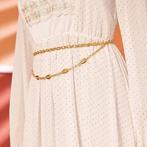 Detail view of a golden double layer waist chain with shell charms on white dress.