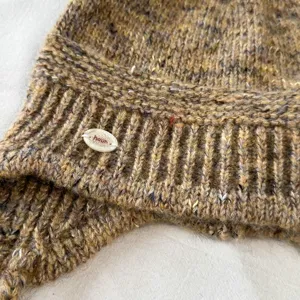 Nahaufnahme der braunen mehrfarbigen Strickmütze zeigt feine Wollstruktur und kleines Etikett.
