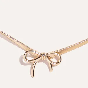 Close-up detail of a luxurious gold metal spring waist chain featuring an elegant bow knot buckle.
