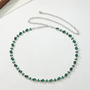 Close-up of elegant women silver waist chain with sparkling green rhinestones and metal links.