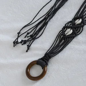 Detailed shot of bohemian handmade black waxed cord woven waist belt with wooden ring and shell.