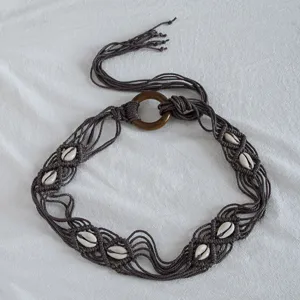 Handmade bohemian braided rope belt detail featuring natural seashells and wooden ring buckle.