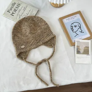 Elegante braune gesprenkelte Strickmütze mit Ohrenklappen und geflochtenen Bändern winterlich.